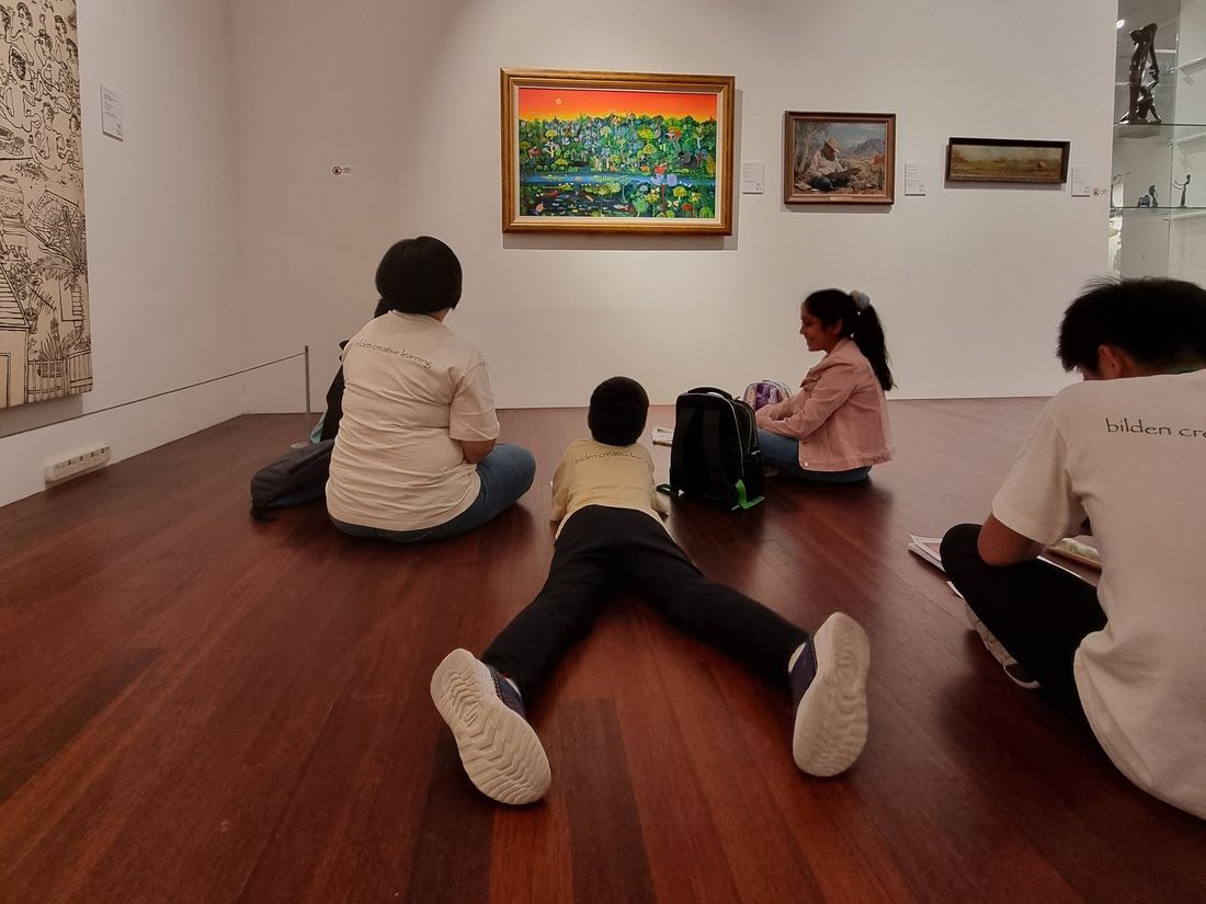Students sitting on a gallery floor studying a painting on the wall