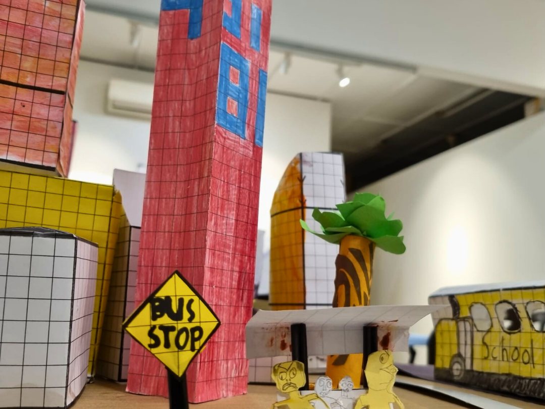 A model city of cardboard tower blocks with a bus stop sign and a school bus